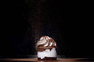 Tezgahın üzerine koyu arkaplan kakao serpilmiş taze pişmiş çikolatalı pastanın yan görüntüsü. Alçakgönüllülük. Kış yiyeceği ve içecek konsepti. Seçici odak.