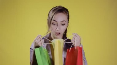 Pastel sarısı arka plan stüdyosundan alışveriş yaptıktan sonra paketleri karıştıran genç bir kız. Halk yaşam tarzı konsepti.