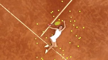 Açık tenis antrenmanından sonra tenis kortunda bir sürü top ve raketle rahatlayan gülümseyen kızın portresi. Dolly vurdu. Üst görünüm