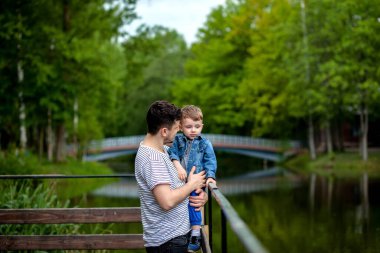 Genç babası ve gülümseyen oğlu parkta kucaklaşıp birlikte vakit geçiriyorlar. Babalar günü kutlaması..