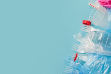 Mavi arkaplanda çeşitli tek kullanımlık plastik atıkların üst görünümü, boşluğu kopyala.