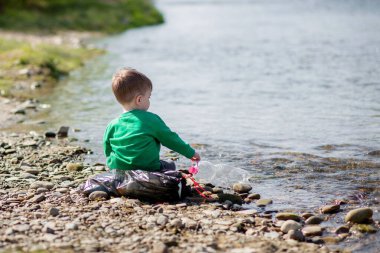 Çevre kavramını kaydedin, küçük bir çocuk çöpleri ve plastik şişeleri toplayıp çöpe atıyor.