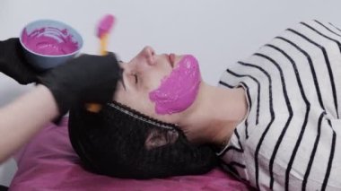 Maske uygulama sürecini değiştir. Spatula tutan bir güzellik uzmanının dişi elleri. Güzellik salonunda cilt bakımı prosedürü. Bir güzellik uzmanının ofisinde kanepede uzanmış bir kadın..