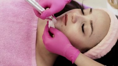 Kozmetik uzmanı, güzellik salonundaki güzel, genç bir kadının yüz derisinin mikro cilt bakımını yapıyor. Kozmetoloji ve profesyonel cilt bakımı.