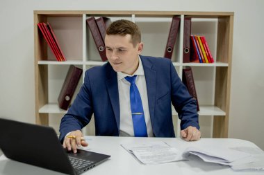 Evde dizüstü bilgisayar ve kağıtlarla çalışan genç bir iş adamı..