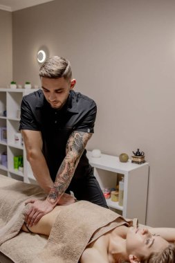 Genç bir kadın karın masajı yaptırıyor. Masör mide masajı yapar.