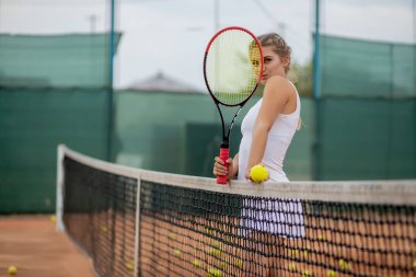 Tenis antrenmanından sonra dinleniyorum. Beyaz üniformalı güzel bir kız ve tenis kortunun yanında spor şapkası..