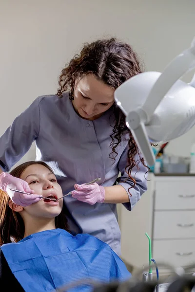 Health check. Dentist in stomatology center is making an examination of woman teeth by using dental tools.