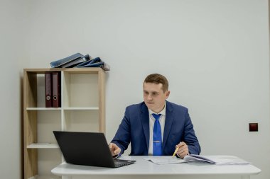 Evde dizüstü bilgisayar ve kağıtlarla çalışan genç bir iş adamı..