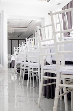 Restorandaki masalarda beyaz sandalyeler, beyaz masa örtüleri.