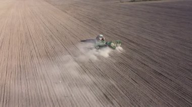 Tarlada tarla süren harrow sistemli traktörün havadan görünüşü. Toz izlerinden oluşan bir sütun. Toprağı yeni ekin ekimi için hazırlıyor..