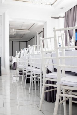 Restorandaki masalarda beyaz sandalyeler, beyaz masa örtüleri..