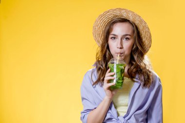 Sarı arka planda plastik bardakla güzel genç bir kadın.