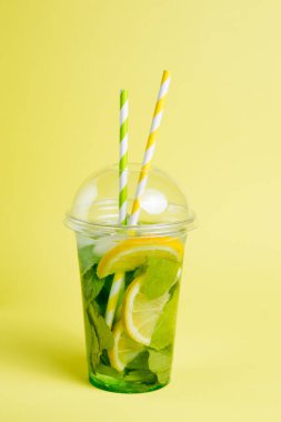 Plastik bardakta mojito kokteyli ve sarı arka planda bir tüp. Paket servis için yaz içeceği. Metin için yer.
