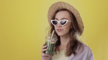 Sarı Stüdyo Üzerindeki Plastik Kupa 'dan Mojito kokteyli içen Şaşırmış Kadın. Yaz içeceği. Soğuk içecek.
