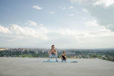 Anne ve oğul güneş doğarken ya da batarken şehrin arka planında balkonda egzersiz yapıyorlar. Sağlıklı yaşam tarzı kavramı..