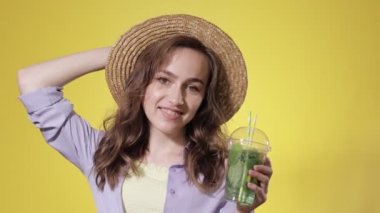 Sarı Stüdyo Üzerindeki Plastik Kupa 'dan Mojito kokteyli içen Şaşırmış Kadın. Yaz içeceği. Soğuk içecek.