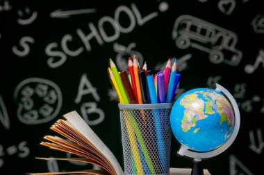 Kitap, kalem ve küre ile okul arka planına yeşil karatahta arka planında beyaz masa üzerinde.