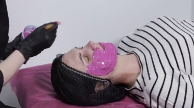 Güzellik uzmanındaki resepsiyonda güzel bir genç kadın, aljinat maskesi, yüze uygulanma süreci, yan görüş. Modern bir güzellik salonunda estetik ameliyat. Kişisel temizlik..
