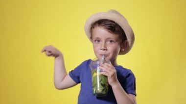 Sarı Stüdyo Üzerindeki Plastik Kupa 'dan Mojito kokteyli içen tatlı çocuk. Yaz, tatil, tatil, güneş, sıcaklık, deniz, sahil.