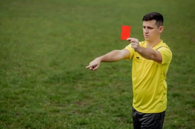 Kızgın futbol hakemi kırmızı kart gösteriyor ve penaltıyı eliyle işaret ediyor..