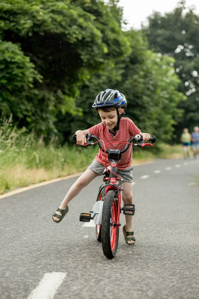Child riding bicycle on the bike path at rain. Kid in helmet learning to ride at summer. Happy boy riding bike, having fun outdoors on nature. Active sport family leisure