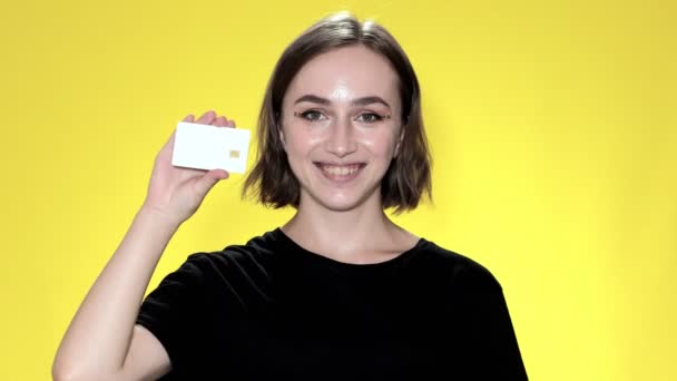 Leende ung kvinna med kreditkort på gul bakgrund — Stockvideo