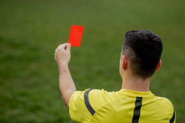 Hakem, hoşnutsuz bir futbol oyuncusu ya da futbolcuya kırmızı kart gösteriyor. Spor anlayışı, kural ihlali, tartışmalı konular, engellerin aşılması
