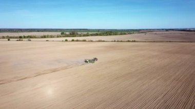 Tarlada tarla süren harrow sistemli traktörün havadan görünüşü. Toz izlerinden oluşan bir sütun. Toprağı yeni ekin ekimi için hazırlıyor..