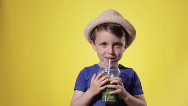 黄色のスタジオを背景にしたプラスチック製のカップからモヒートカクテルを飲むかわいい男の子 ビーチ — ストック動画