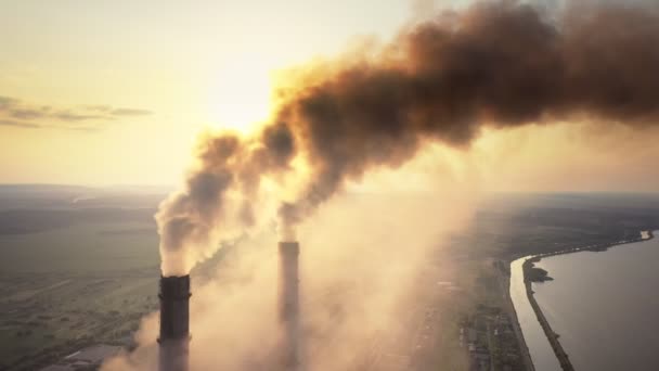 Воздушный обзор высоких труб угольной электростанции с черным дымом, движущимся вверх загрязняющей атмосферу на закате. — стоковое видео