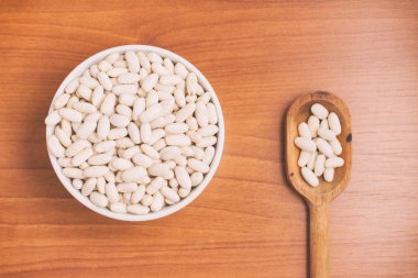  Bir kase ve ahşap bir masa üzerine kaşık içine beyaz fasulye. Phaseolu