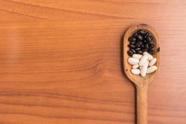 Frijoles crudos blancos y negros en una cuchara sobre una mesa de madera . — Foto de Stock