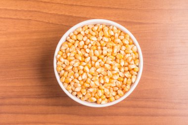 Ahşap bir masa üzerinde bir kaseye ham Mısır taneleri.