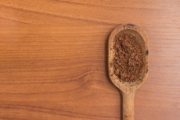 Cacau em pó em uma colher sobre uma mesa de madeira . — Fotografia de Stock