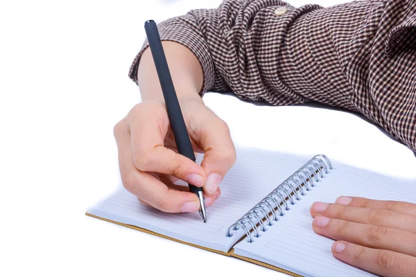 Une main d'enfant écrit avec un stylo sur un cahier en spirale sur fond blanc — Photo