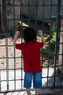 Metal parmaklıklar tutan küçük mutlu çocuk