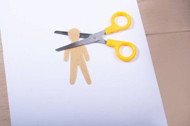 Kağıt adamın kafasını kesen makas tahta arka planda beyaz kağıt üzerinde