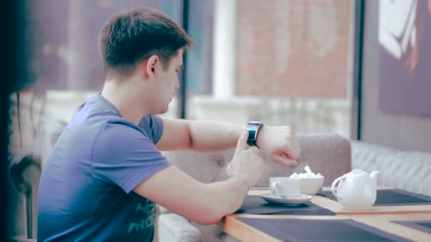 Schöner Mann mit Smartwatch sitzt in Café in der Stadt. — Stockvideo