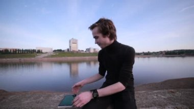 Genç adam getting haber tablet bilgisayar ile şehir göl kenarında.