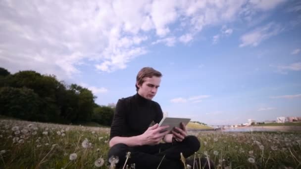 Jovem com computador tablet sentado no parque, conversando, surfando, estudando . — Vídeo de Stock