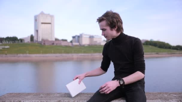 Молодий чоловік отримує повідомлення з планшетним комп'ютером біля міського озера . — стокове відео