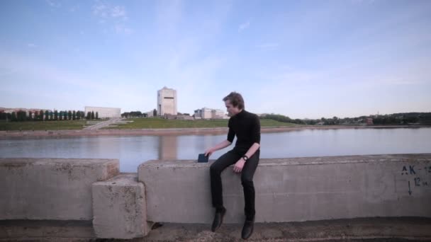 Jongeman getting depêche met tablet pc in de buurt van het meer van de stad. — Stockvideo