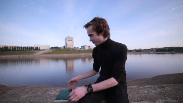 Genç adam getting haber tablet bilgisayar ile şehir göl kenarında. — Stok video