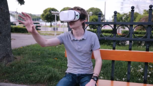 Young man with 3D VR head mounted display in park watching 360 movies, playing VR games. — Stock Video