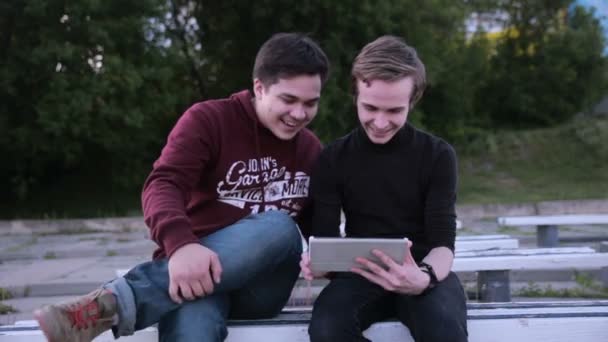 Two male friends with tablet computer talking surfing outdoors. — Stock Video