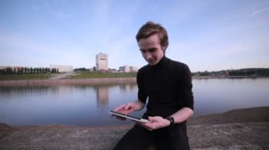 Genç adam getting haber tablet bilgisayar ile şehir göl kenarında.