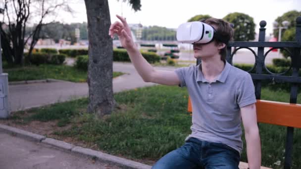 Jonge knappe man met VR-bril zitten in een stadspark. — Stockvideo