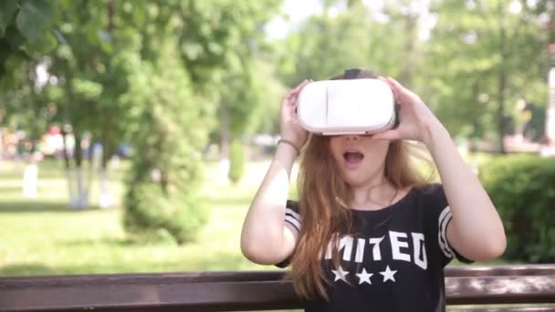 Knap meisje op zoek in virtual reality bril zitten in park, buitenshuis. — Stockvideo
