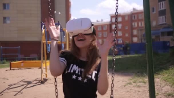 Девушка в очках виртуальной реальности, смотрящая видео в 360 градусном шлеме виртуальной реальности сидя на качелях . — стоковое видео